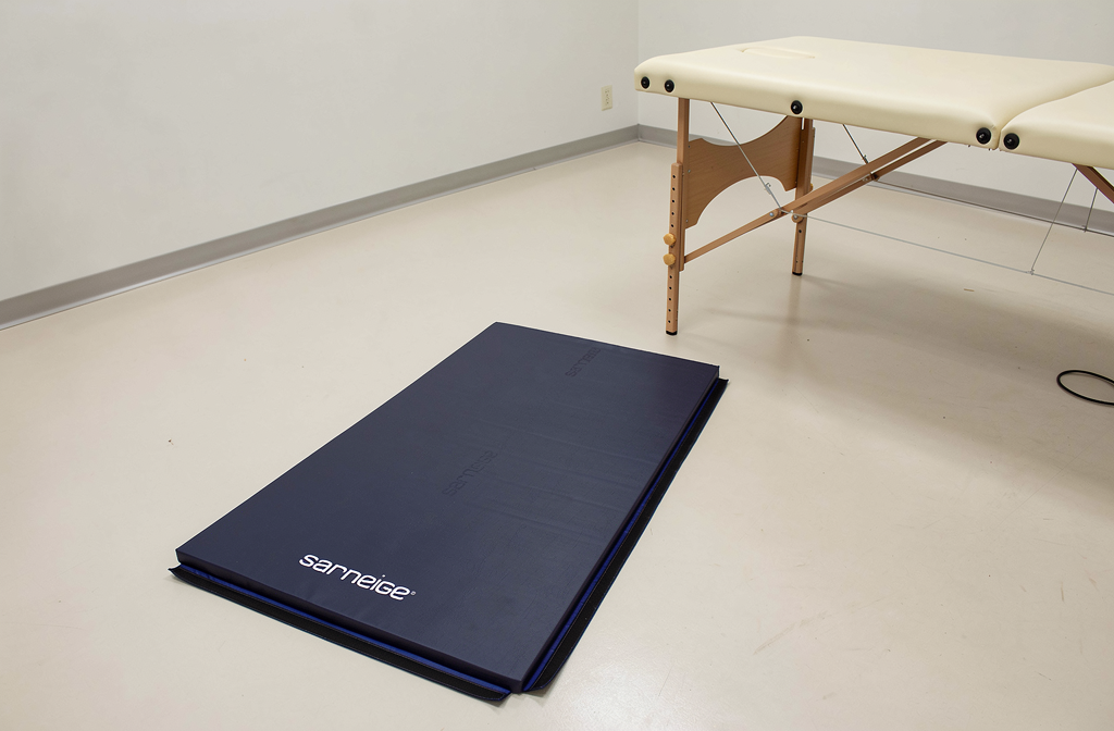 Blauwe therapiemat op de vloer naast een behandeltafel voor coördinatieoefeningen.
