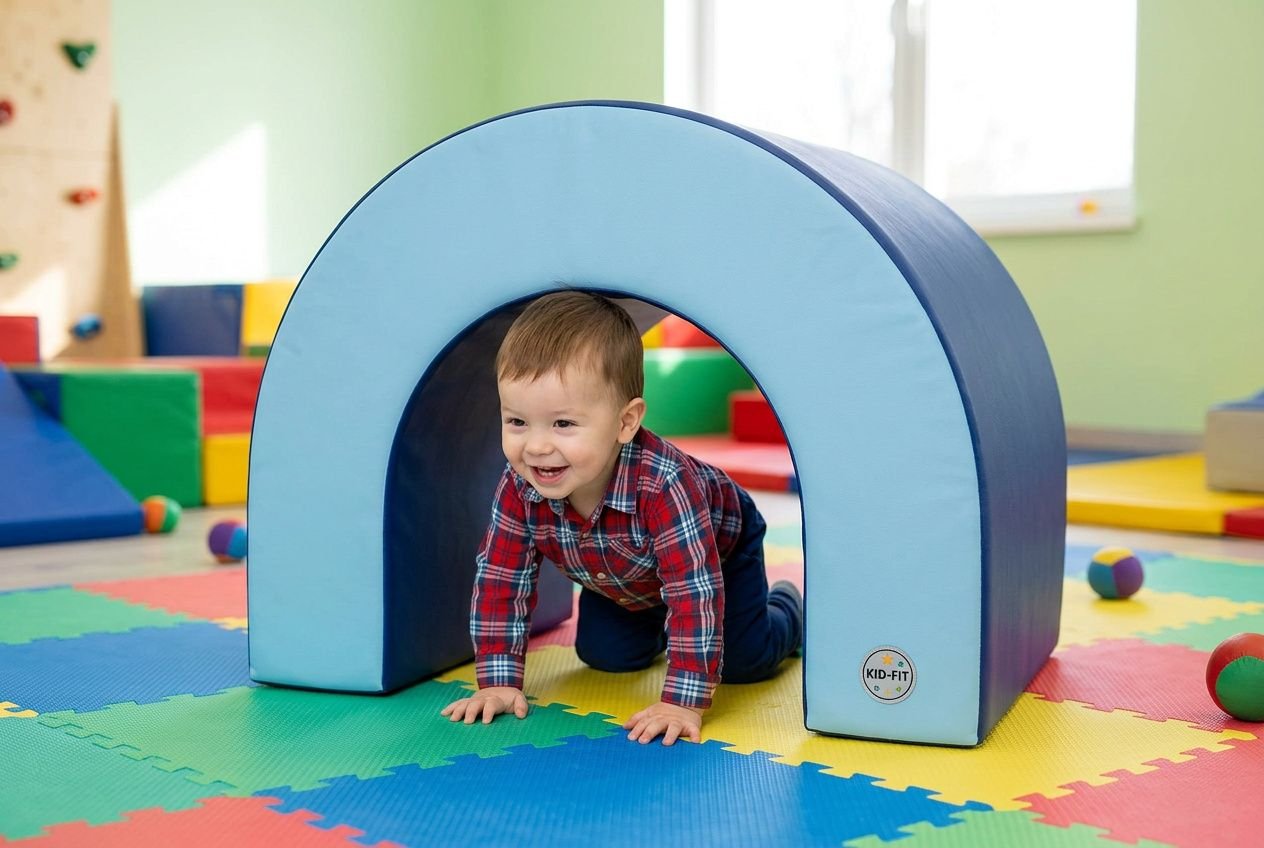 Kleine peuter kruipt door een zacht blauw tunnelvormig psychomotoriek materiaal voor kinderen in een speelhoek met kleurrijke speelmatten.