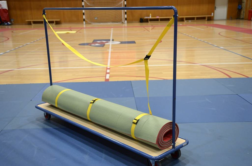 Rolmat op wieltjes met gele draagbanden in een sporthal, klaar voor judomattraining.