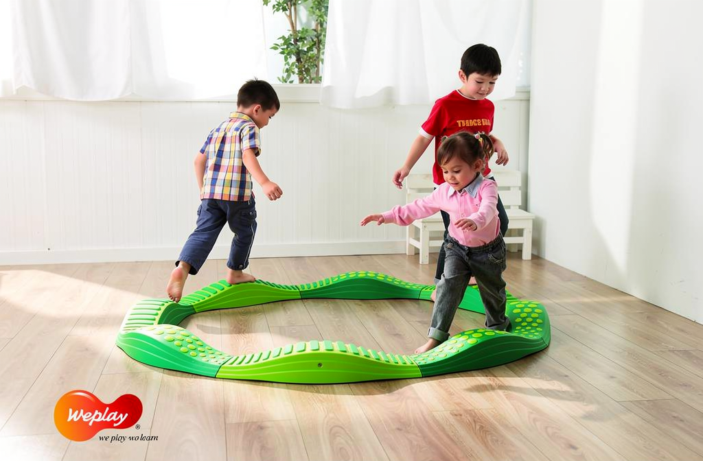 Trois enfants jouent sur un parcours d’équilibre vert en intérieur, promouvant l’activité équilibre enfant.